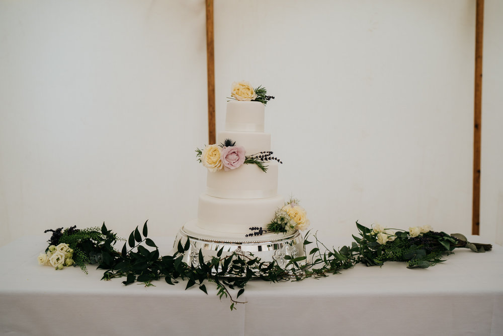  Photograph of three-tiered, white wedding cake with yellow and pink roses as decoration 