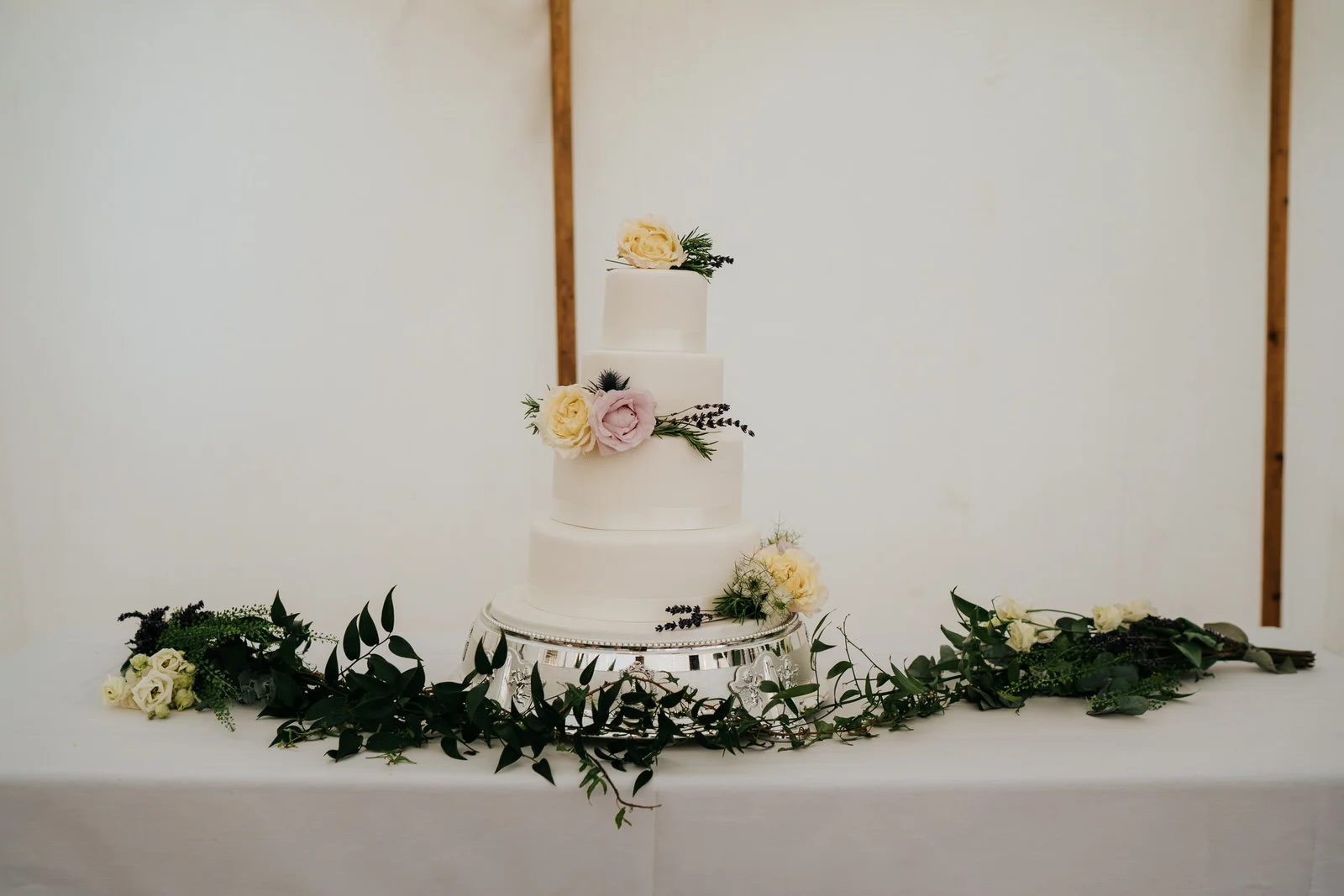 Photograph of three-tiered, white wedding cake with yellow and pink roses as decoration