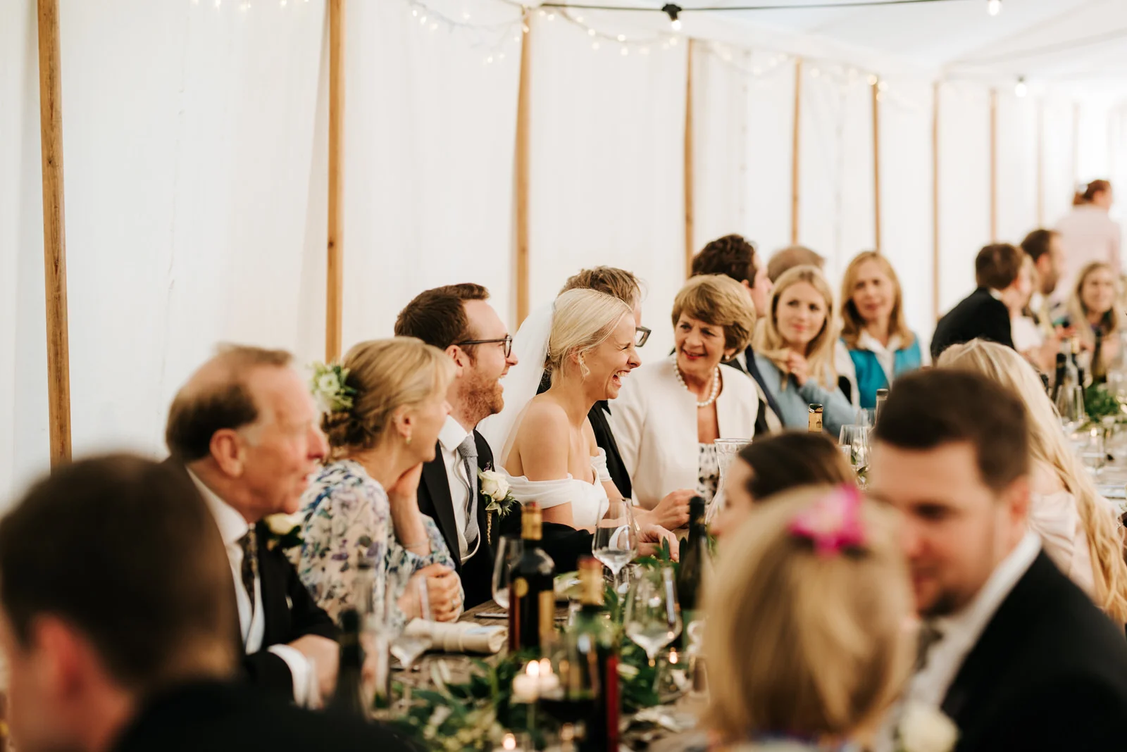 Wide photograph of the head table during the wedding breakfast with bride in the middle, in focus, smiling