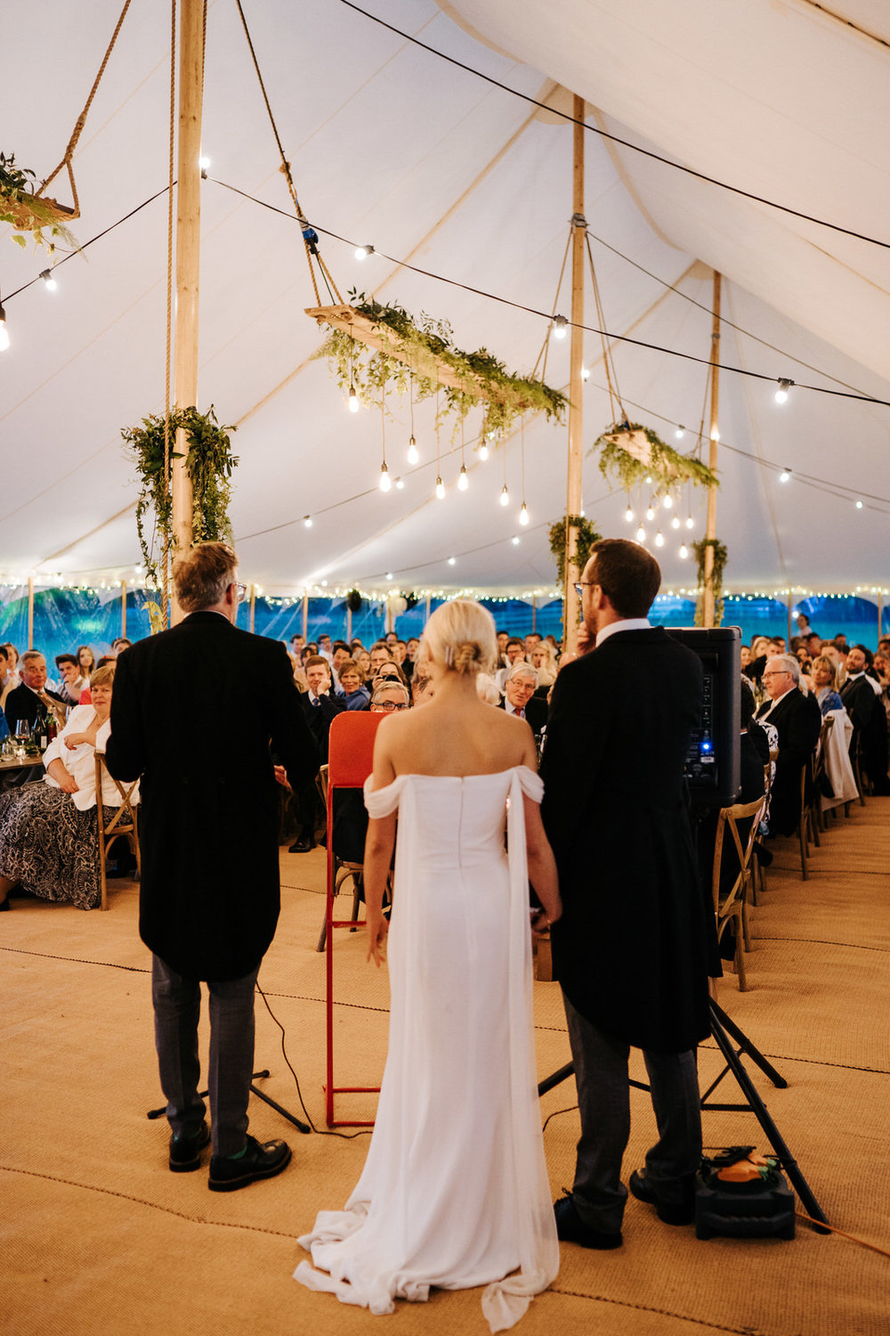  Wide photograph of the father of the bride delivering his speech as guests listen attentively inside marquee at Hawarden Castle, Wales 