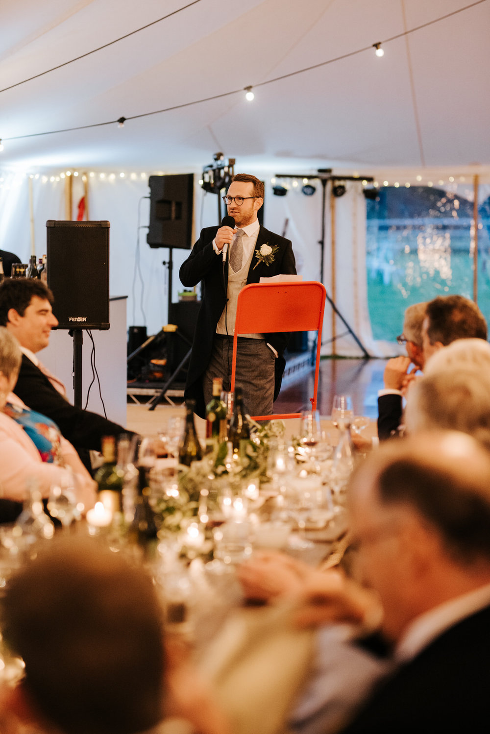  Groom delivers his wedding speech while standing at podium with guests in front 