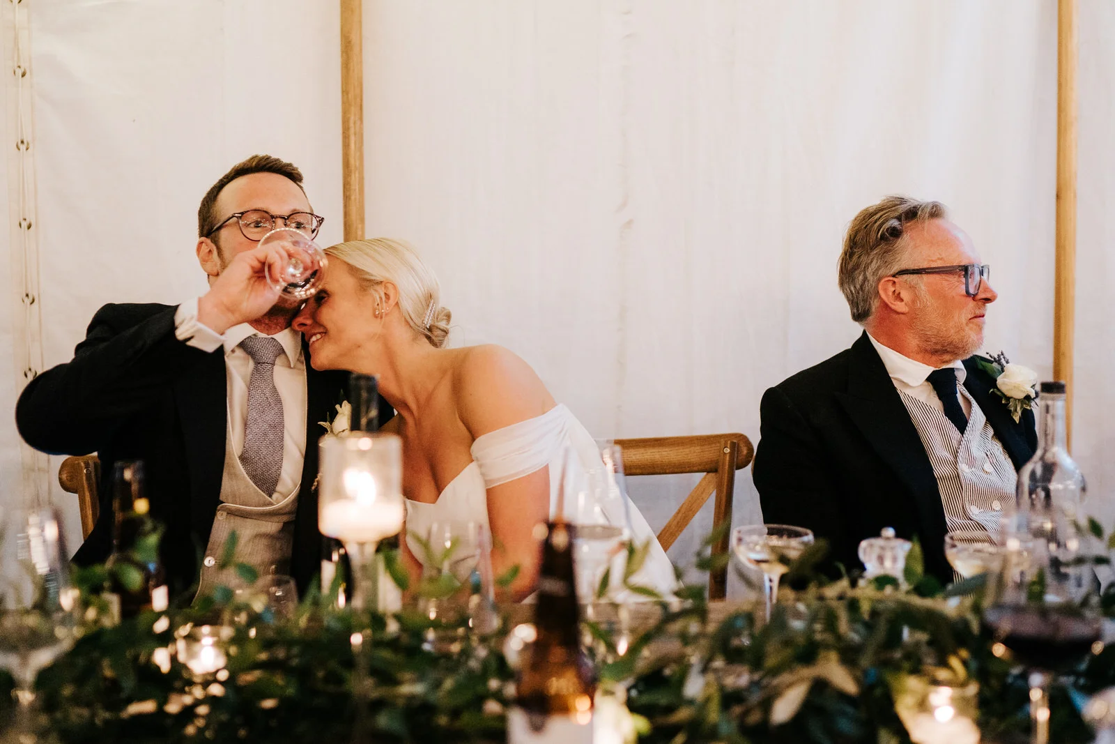 Bride embraces groom, as he takes a drink of wine, after he has completed his speech