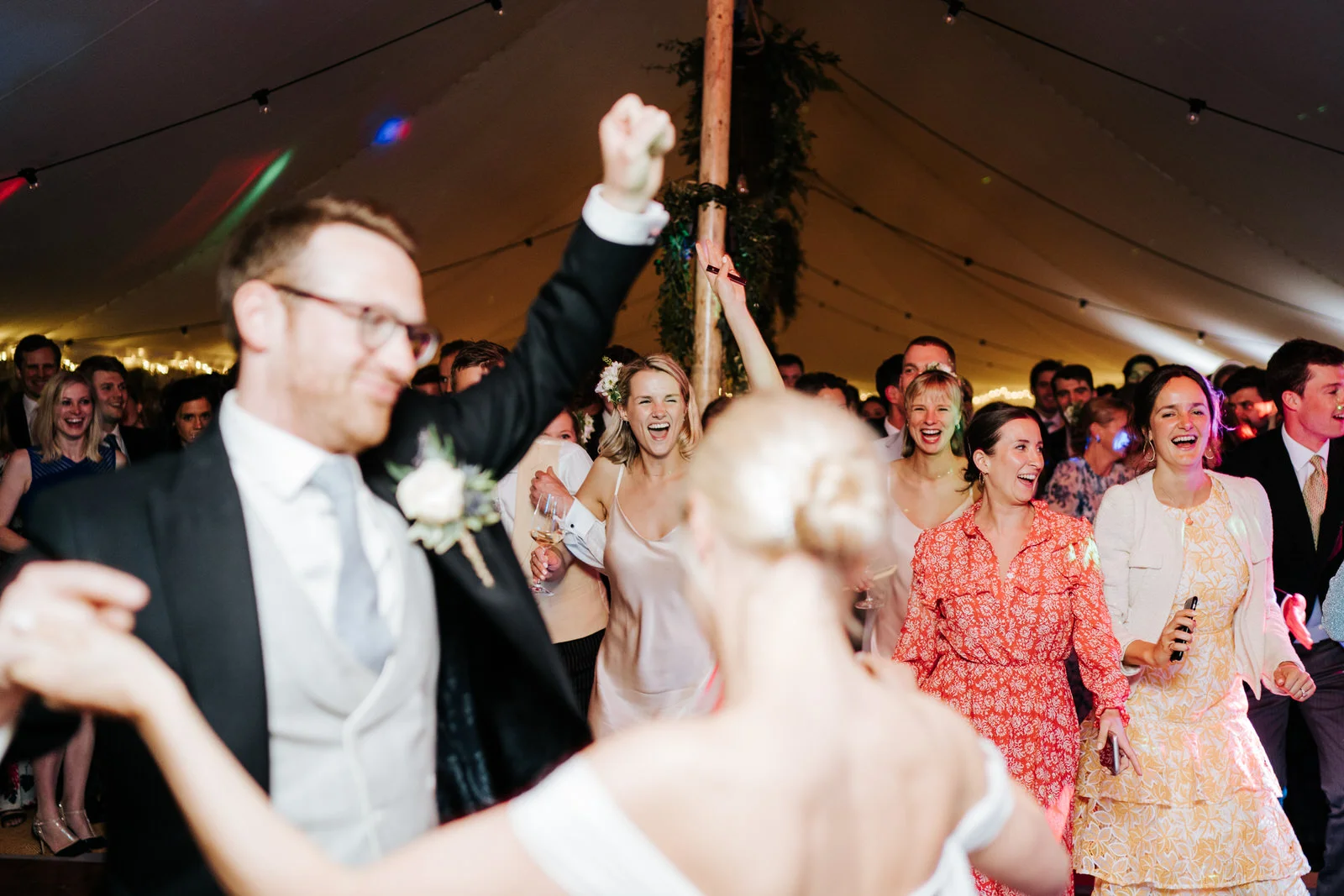 Bride and groom, out of focus in front, finish their first dance and invite guests onto the dancefloor