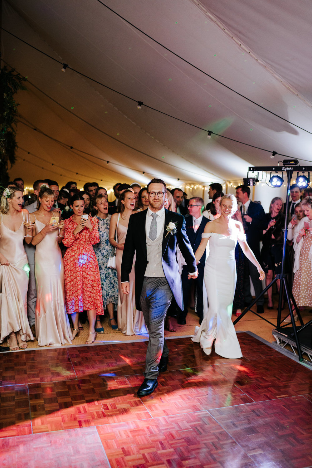  Bride and groom hold hands and walk onto dancefloor to have their first dance 