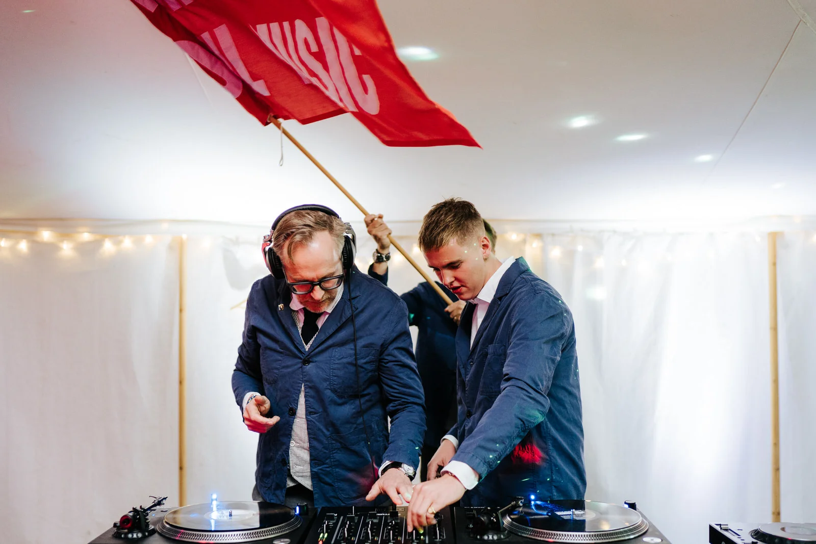 Father of the bride and brothers of the bride DJing behind the decks and waving a big red fan