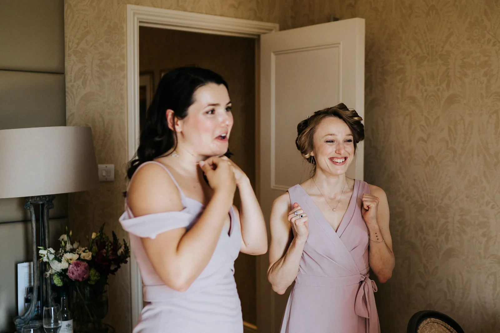Two bridesmaids raise their hands in excitement as bridesmaid finishes getting ready