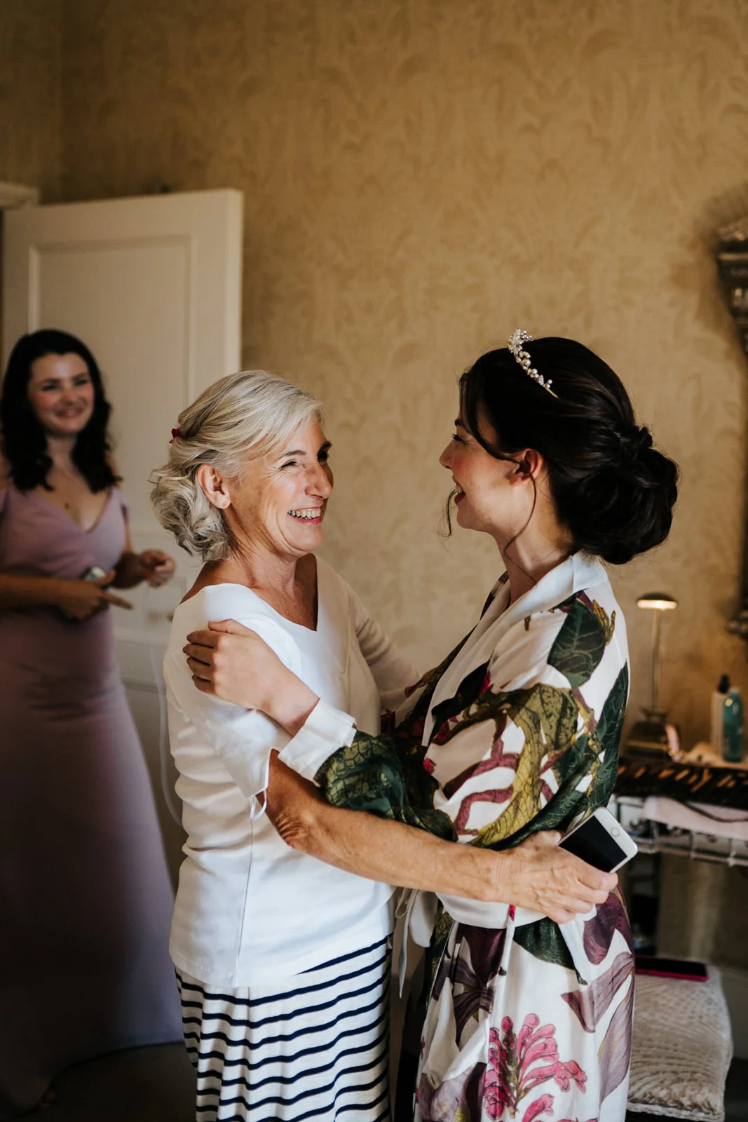 Mother of the bride and bride hug and smile at each other