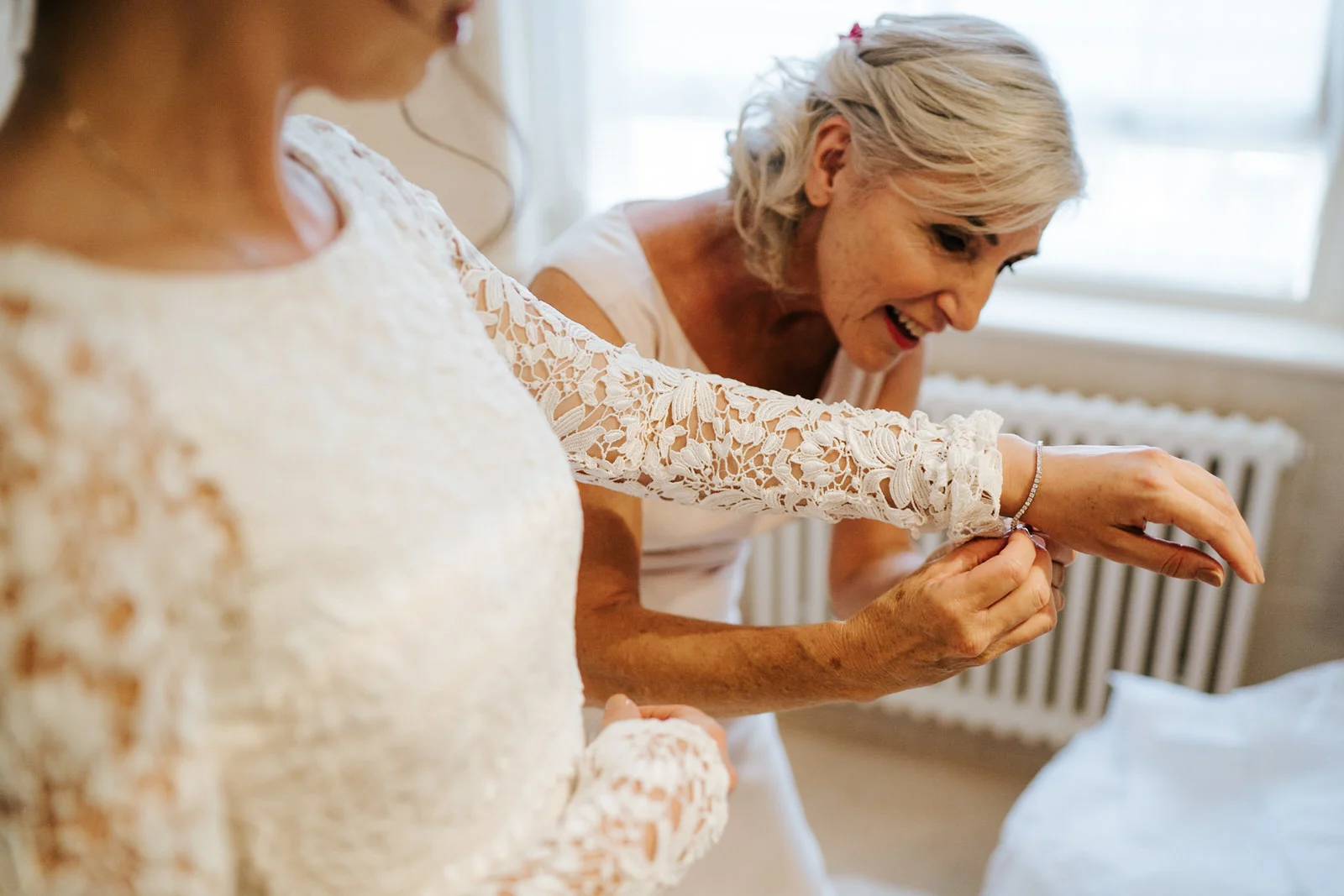 Mother of the bride helps bride put on a bracelet as she finishes getting in her dress