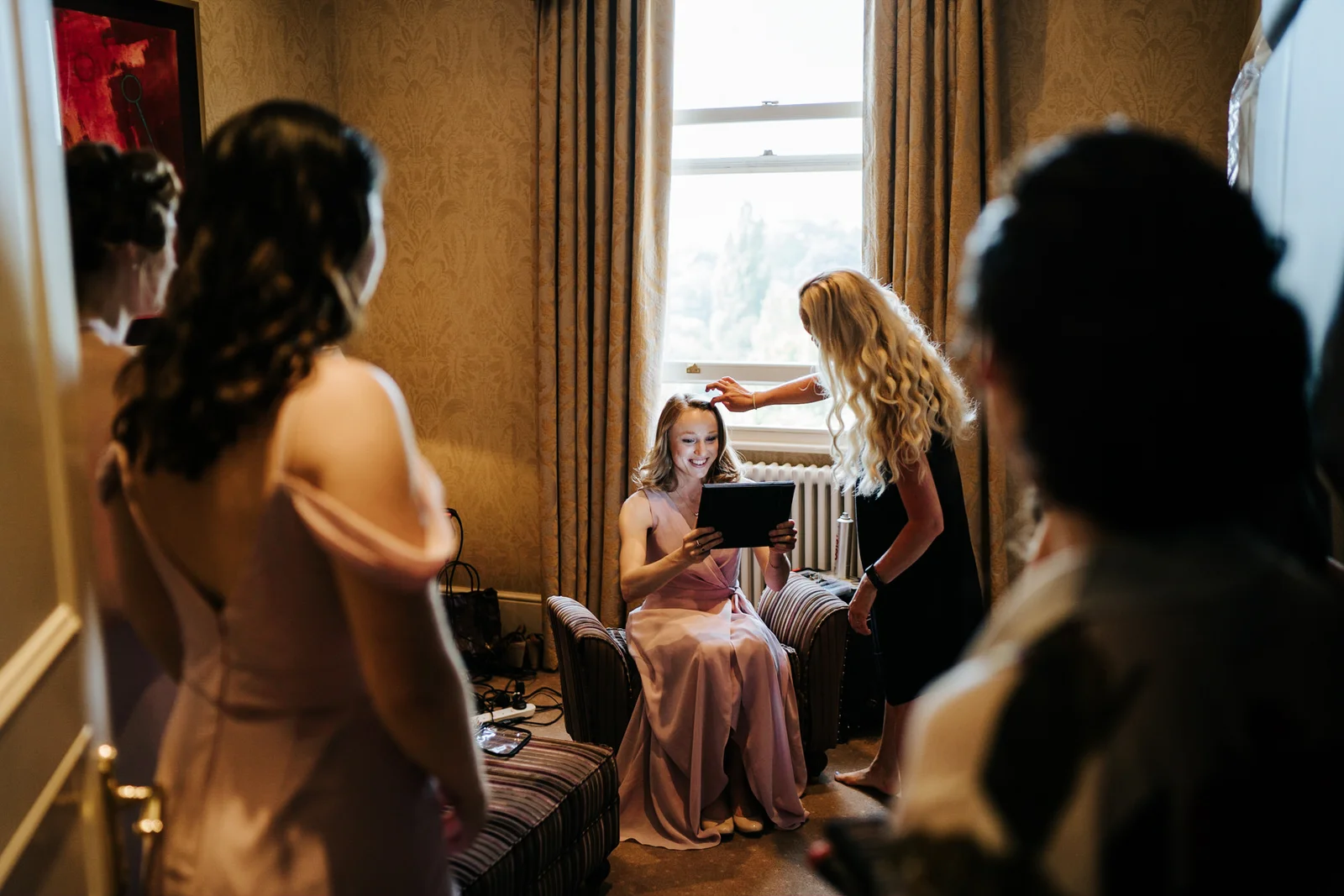 Bridesmaid is sitting and finishes her hair and makeup as other bridesmaids look at her