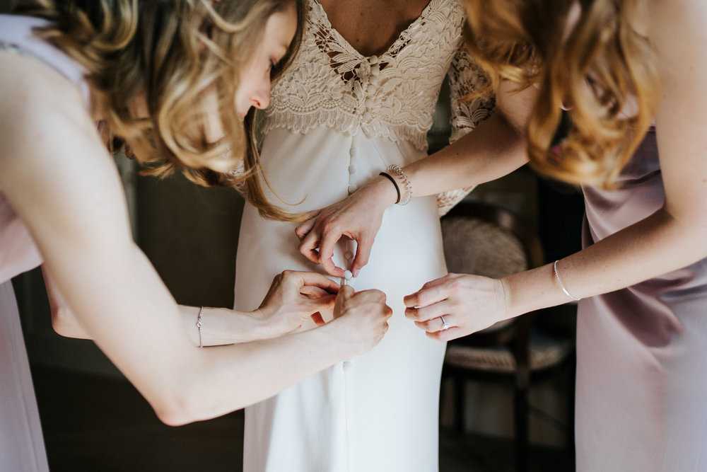  Bridesmaids finish helping bride into her dress by doing buttons up at the back 