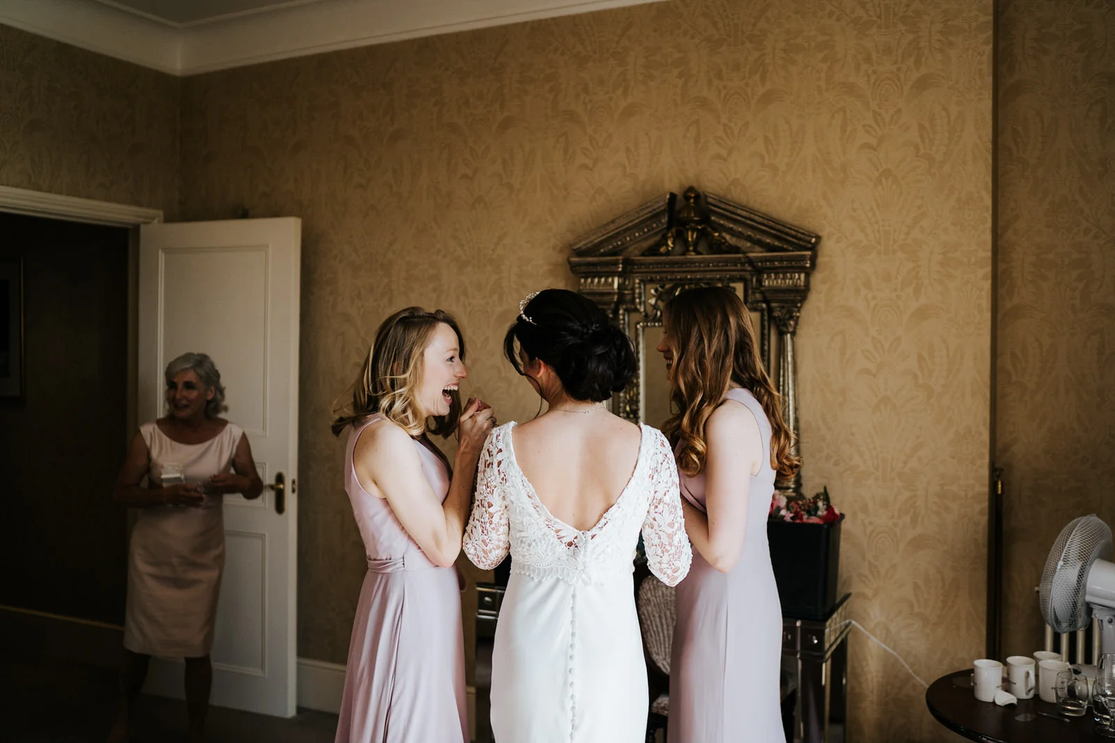 Bridesmaids stand with the bride and look at each other in excitement as they are about to leave for the wedding ceremony