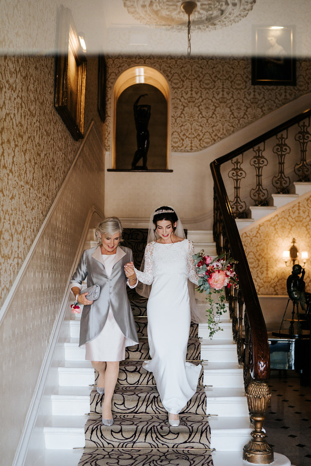  Mother of the bride and bride walk down the stairs of the petersham hotel in richmond and head towards wedding car 