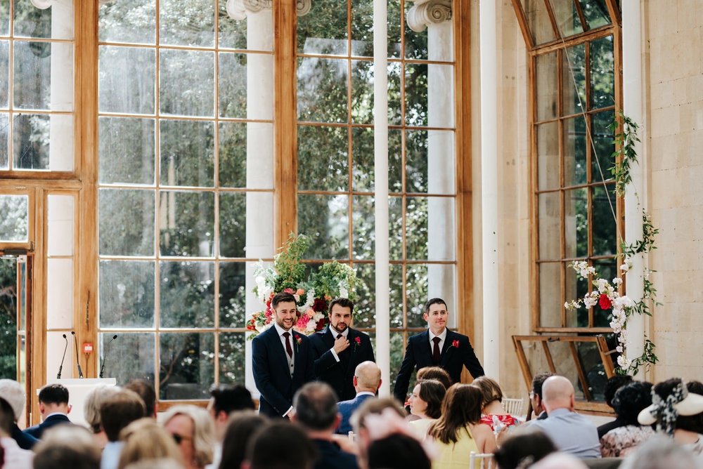  Groom and two gromsmen stand at the front of the aisle at Nash Conservatory in Kew Gardens waiting for the bride to arrive 