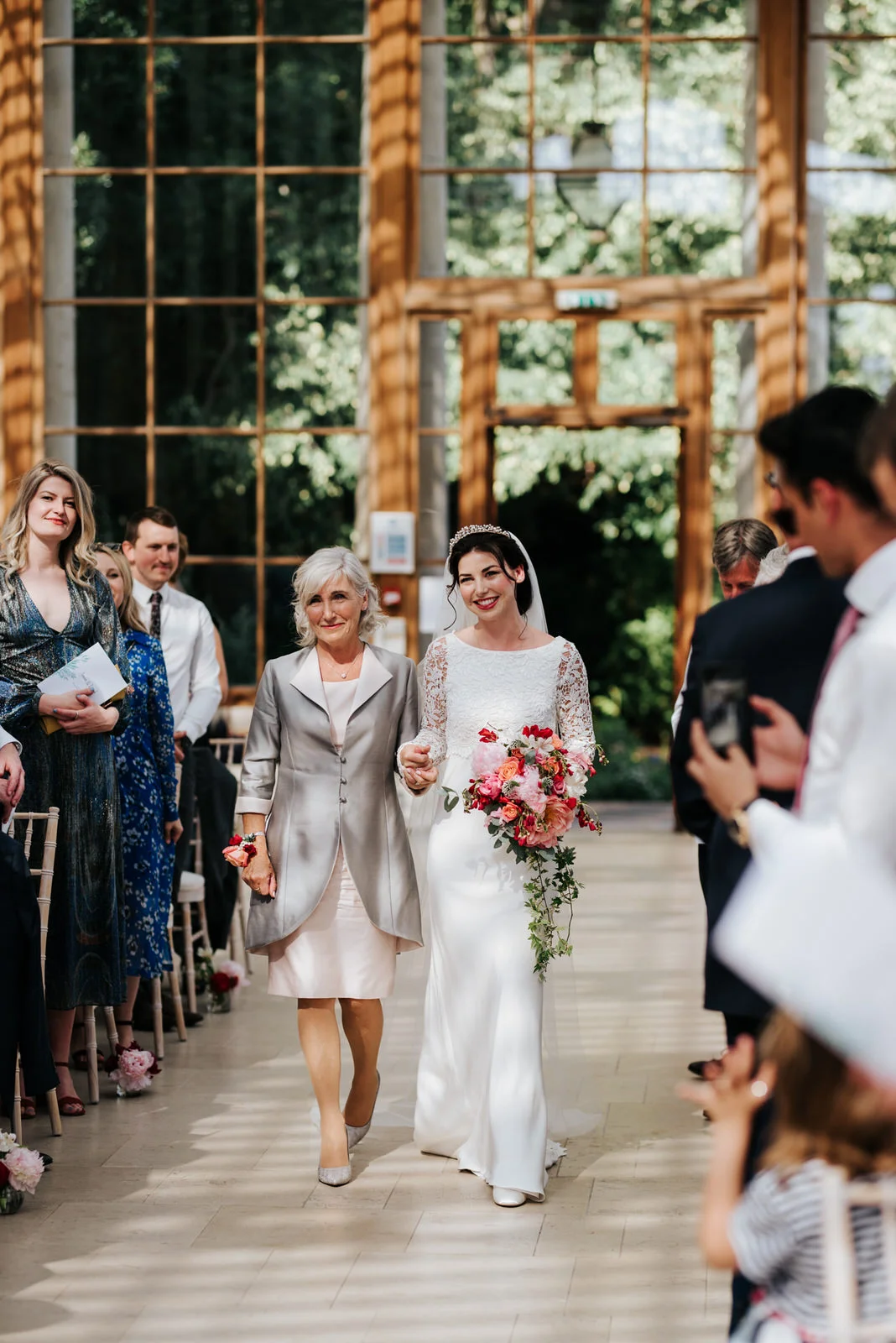 Bride and mother of the bride walk down the aisle looking emotional and excited