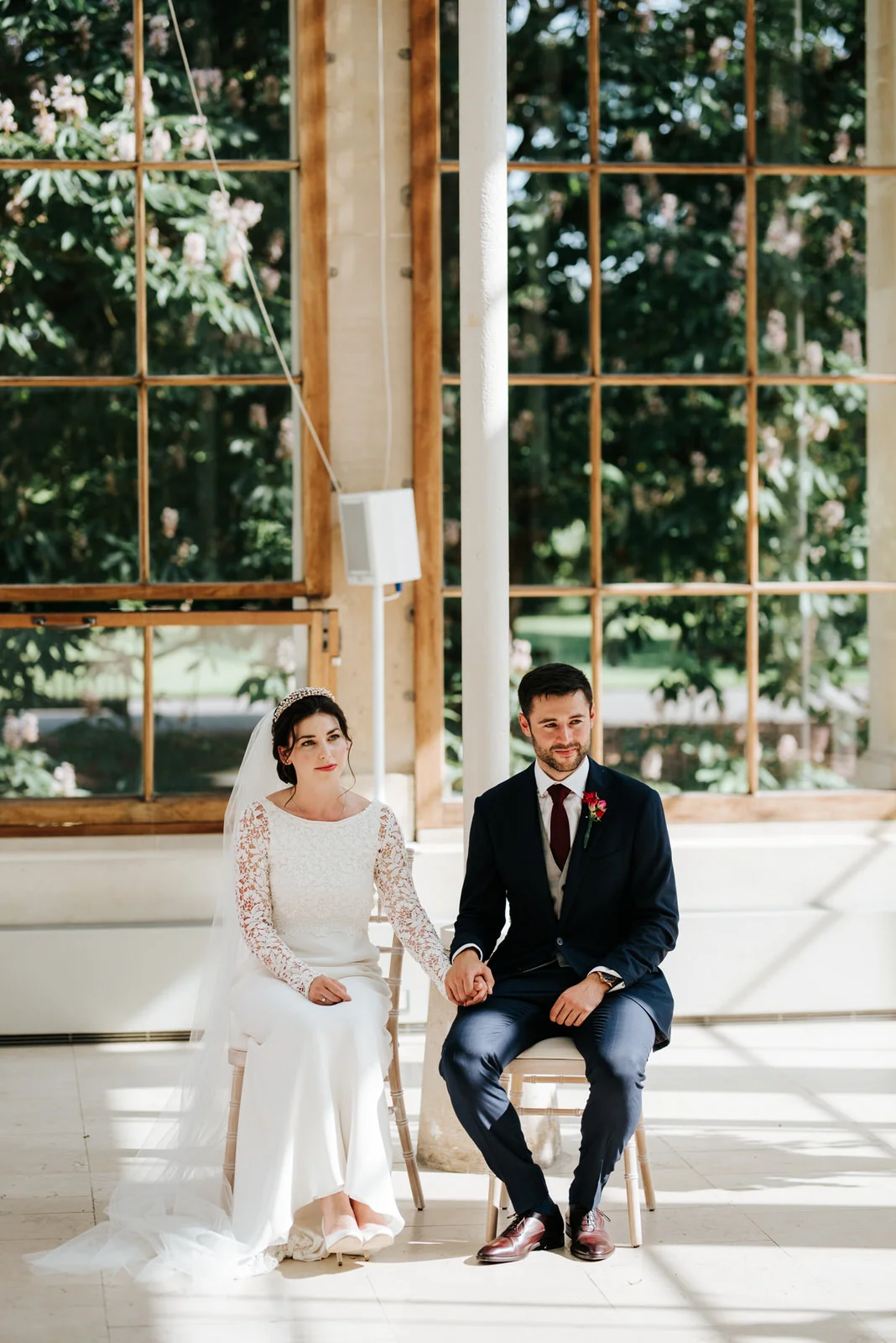 Bride and groom sit and hold hands as they listen to readings during wedding ceremony at Nash Conservatory in Kew Gardens