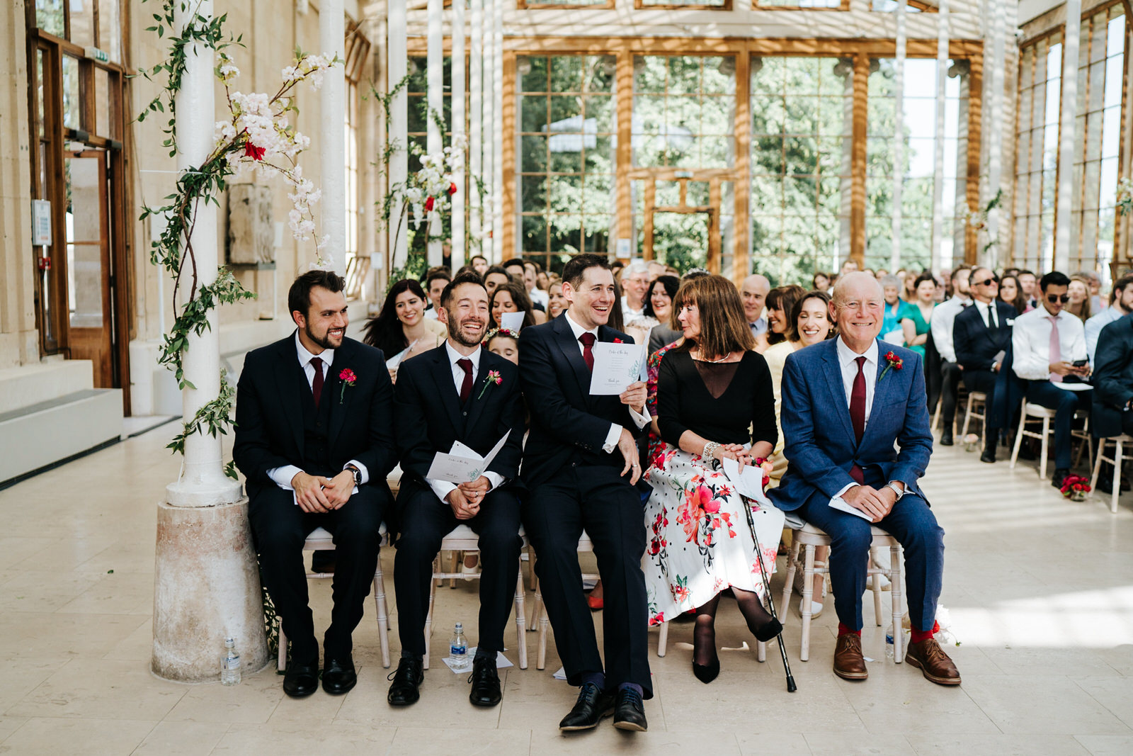  Grooms brothers, groomsmen and parents sit in the first row and smile 