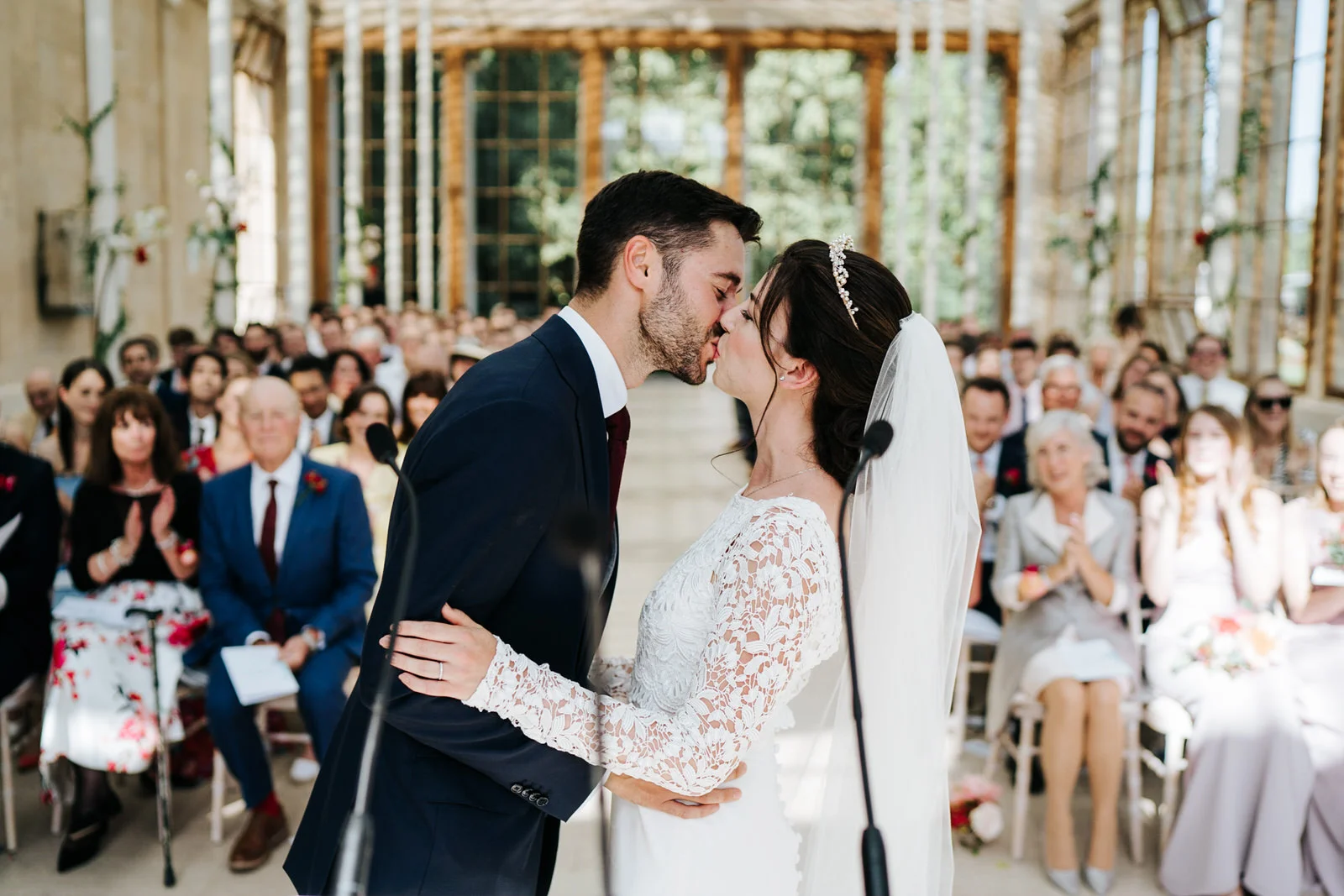 First kiss at nash conservatory wedding at Kew Gardens while guests, out of focus, look from the back.