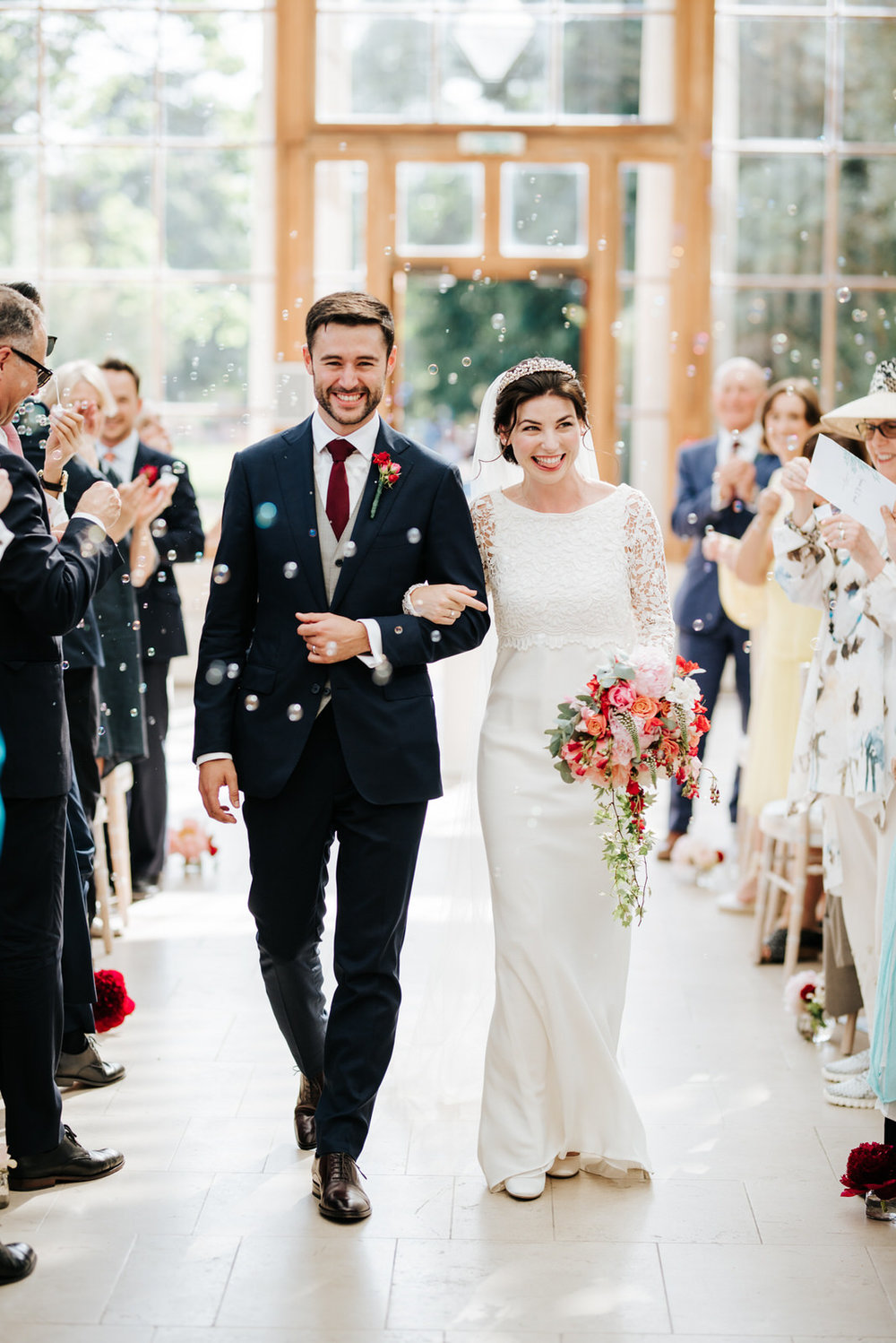  Bride and groom walk back down the aisle as a married couple while guests blow bubbles at them 