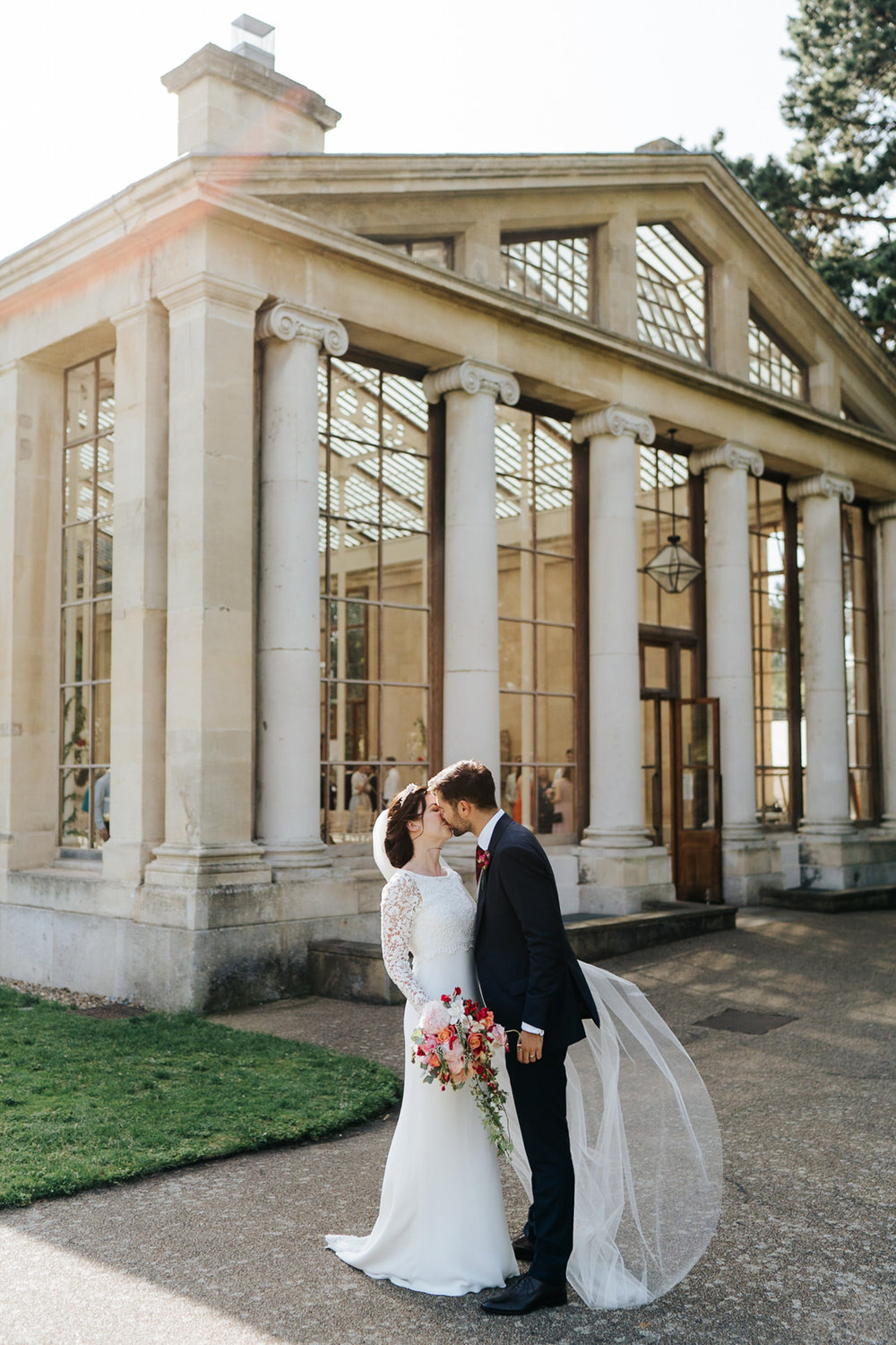  Bride and groom pose for a photograph and kiss outside of Nash Conservatory at Kew Gardens 