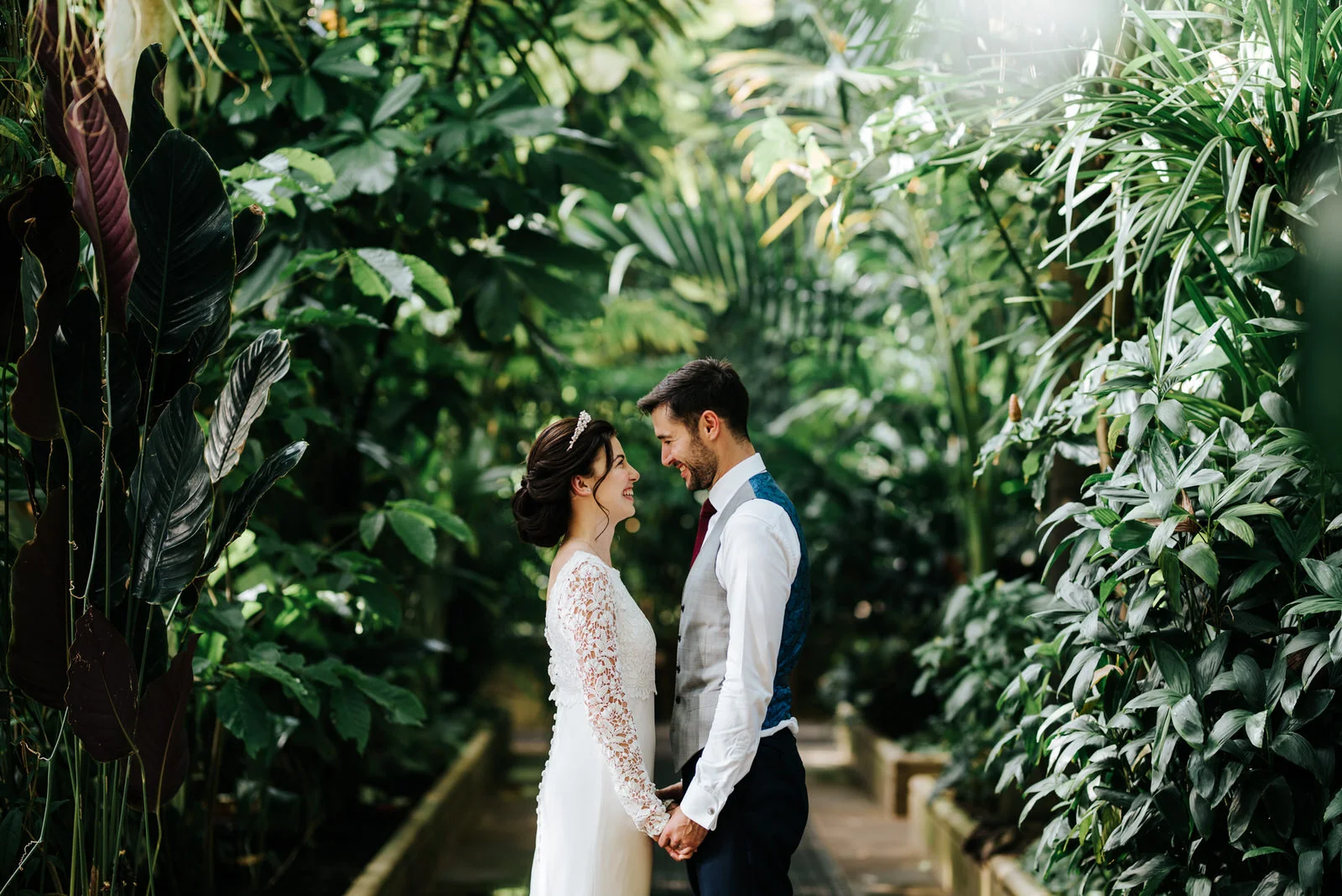 bride and groom look at each other and hold hands for a posed photograph inside the Palm House at Kew Gardens