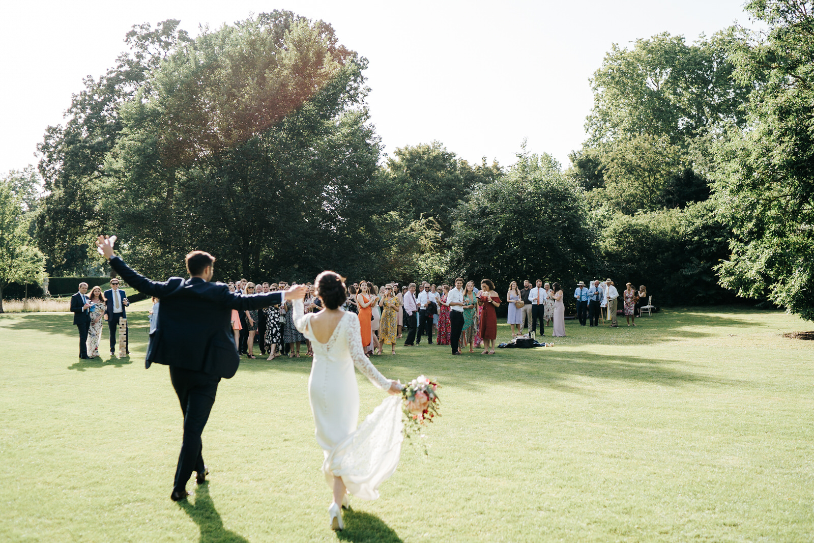  Bride and groom hold hands up in the air and walk towards all their guests during drinks reception 