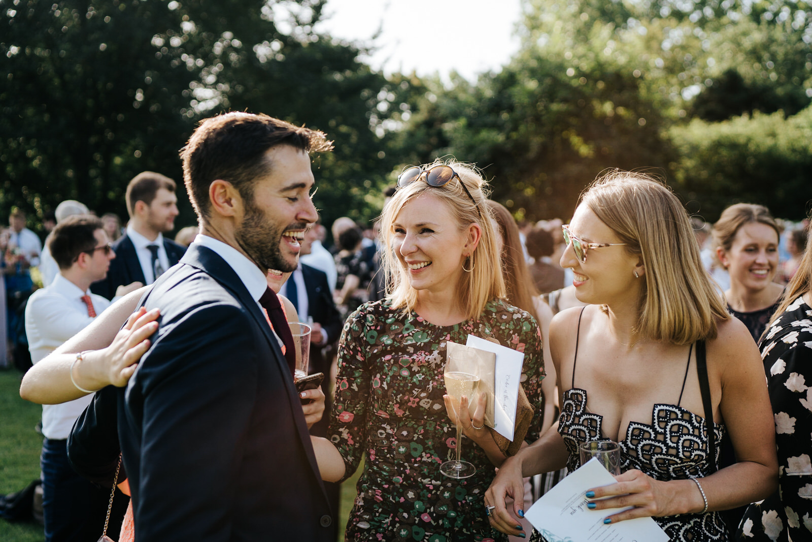  Groom talks to and smiles with a few guests during the wedding drinks reception at Kew Gardens 