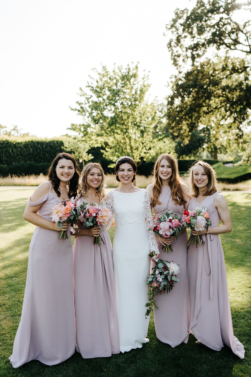  Bride and bridesmaids stand in beautiful light as they look at camera for a posed photograph 