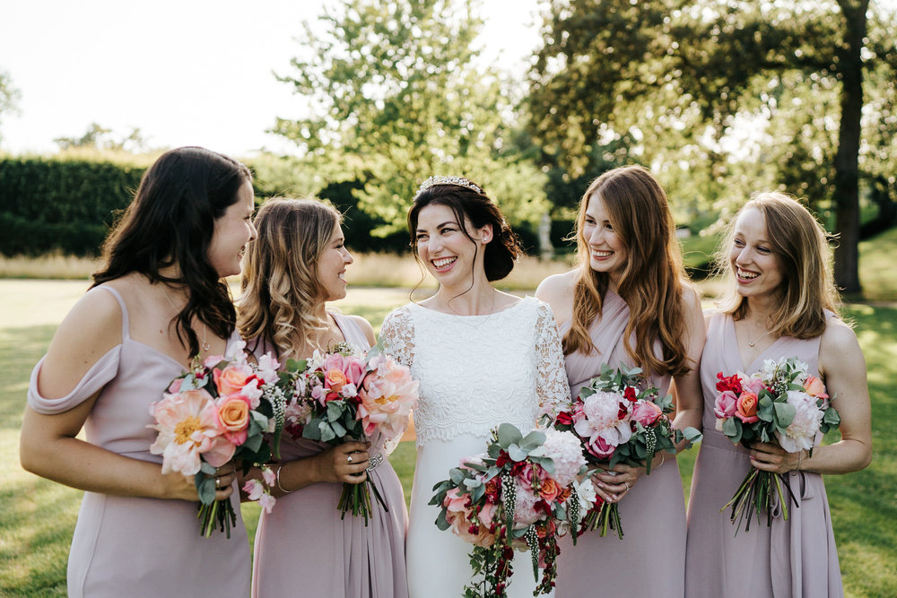  Bride and bridesmaids stand in beautiful light as they look at each other for a posed photograph 