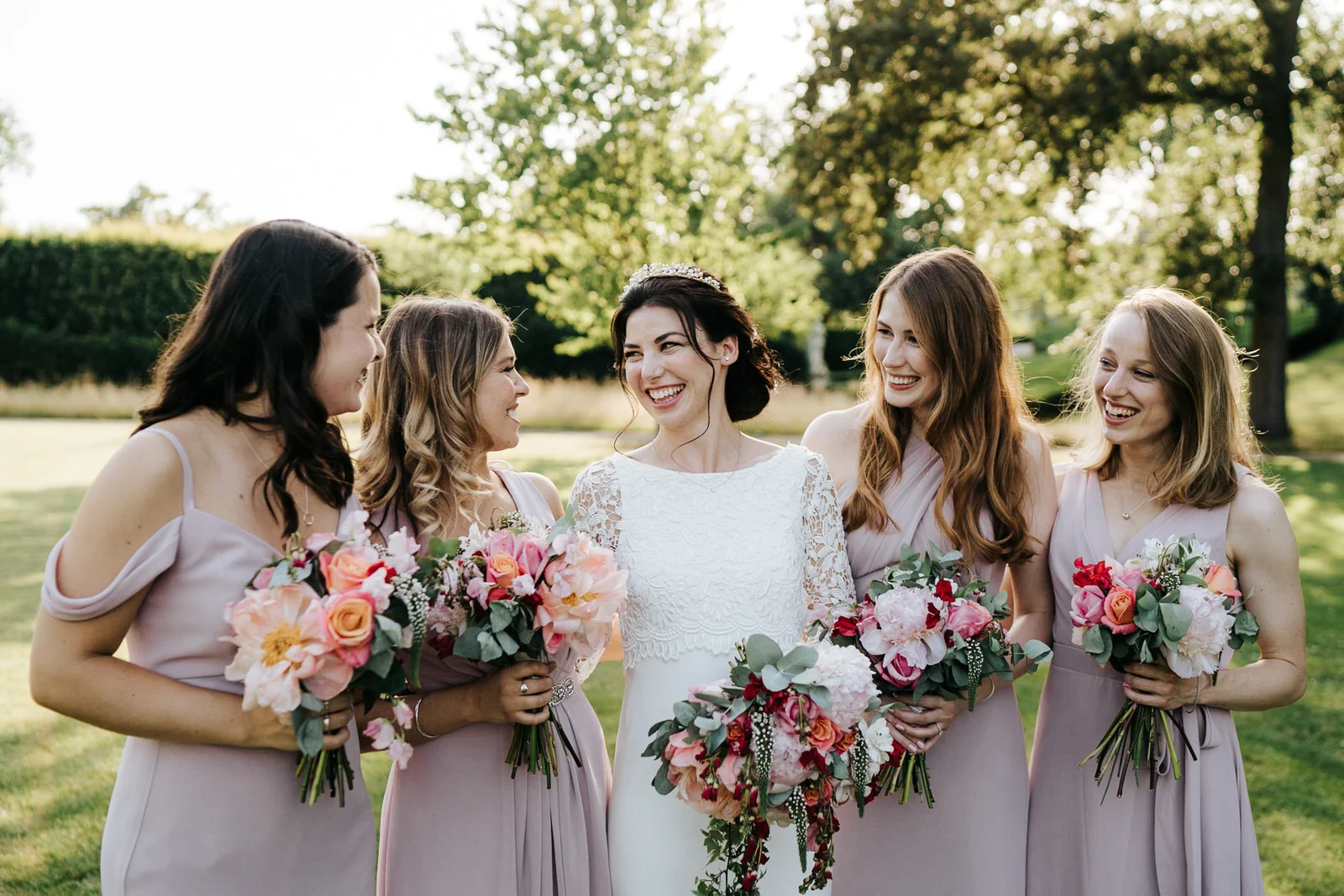 Bride and bridesmaids stand in beautiful light as they look at each other for a posed photograph