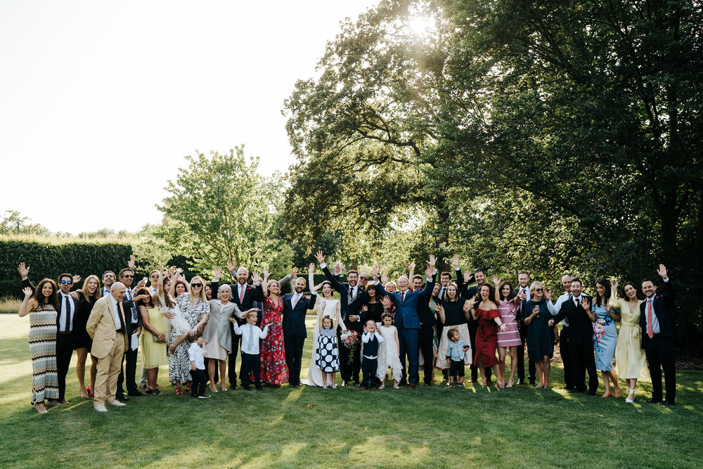  Group photograph of bride and grooms family putting their hands in the air 