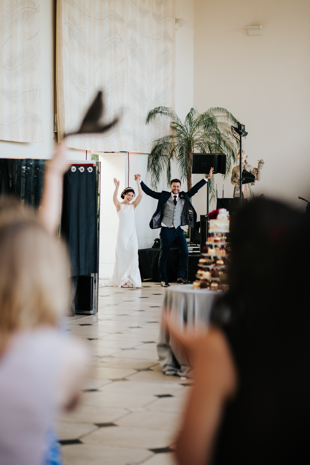  Bride and groom make their epic entrance with hands in the air at the orangery at kew gardens as guests clap and wave napkins 