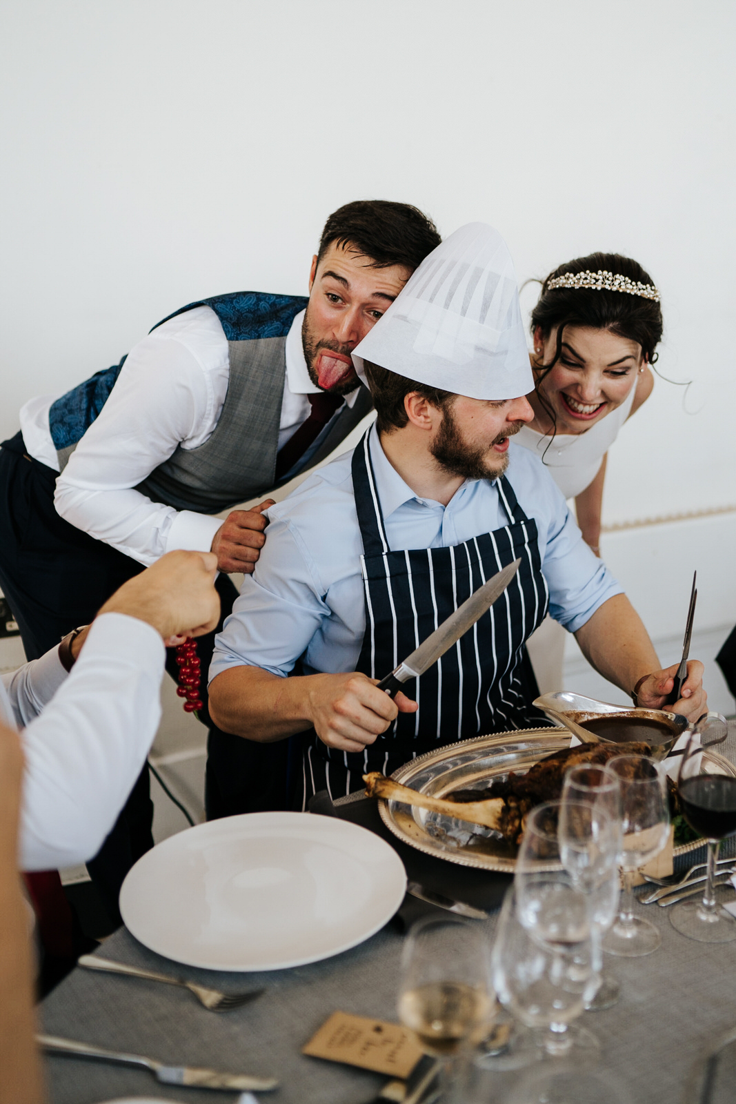  Bride and groom make funny faces at one of the guests carving the meat for his table 