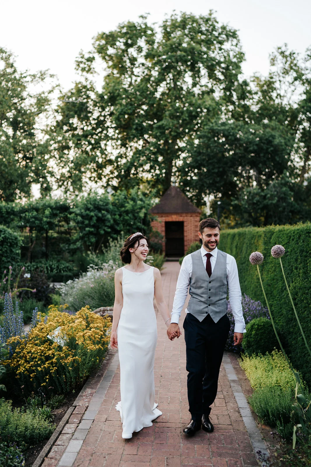 Bride and groom hold hands and walk around the gardens of kew palace in golden evening light