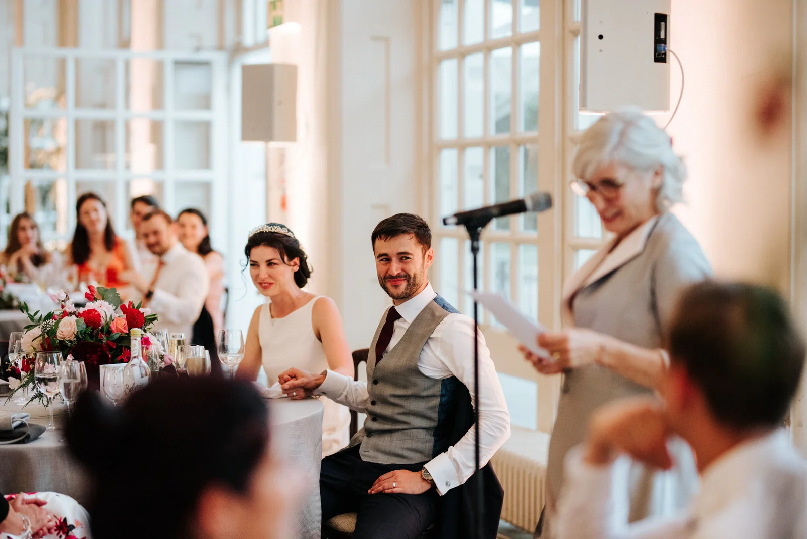 Bride and groom hold hands and listen to speech of the mother of the bride