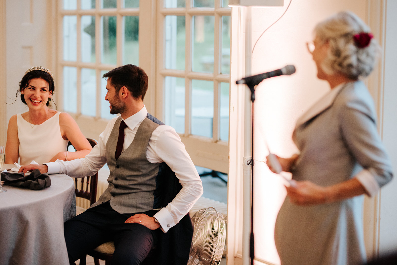  Bride and groom hold hands and look at each as they listen to speech of the mother of the bride 