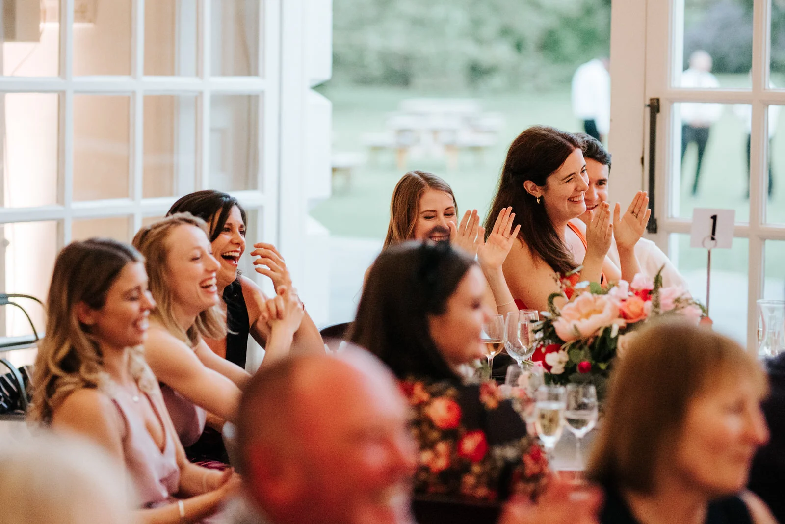 Guests and bridesmaids clap and smile as they react to mother of the bride speech