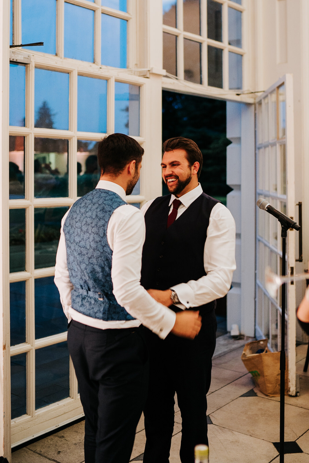  Best man and groom look at each other and smile as best man finishes speech 