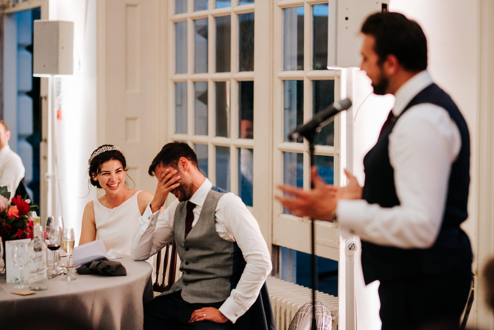  Best man delivers his speech as bride smiles at groom and groom covers his face in embarrasment 