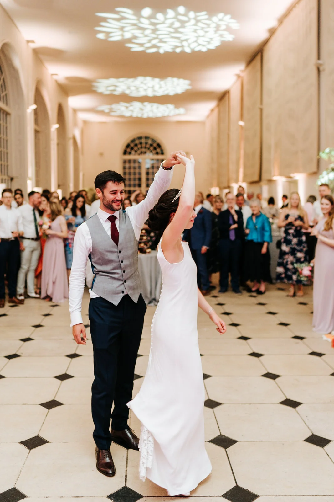 Bride and groom have their first dance as guests look from the back