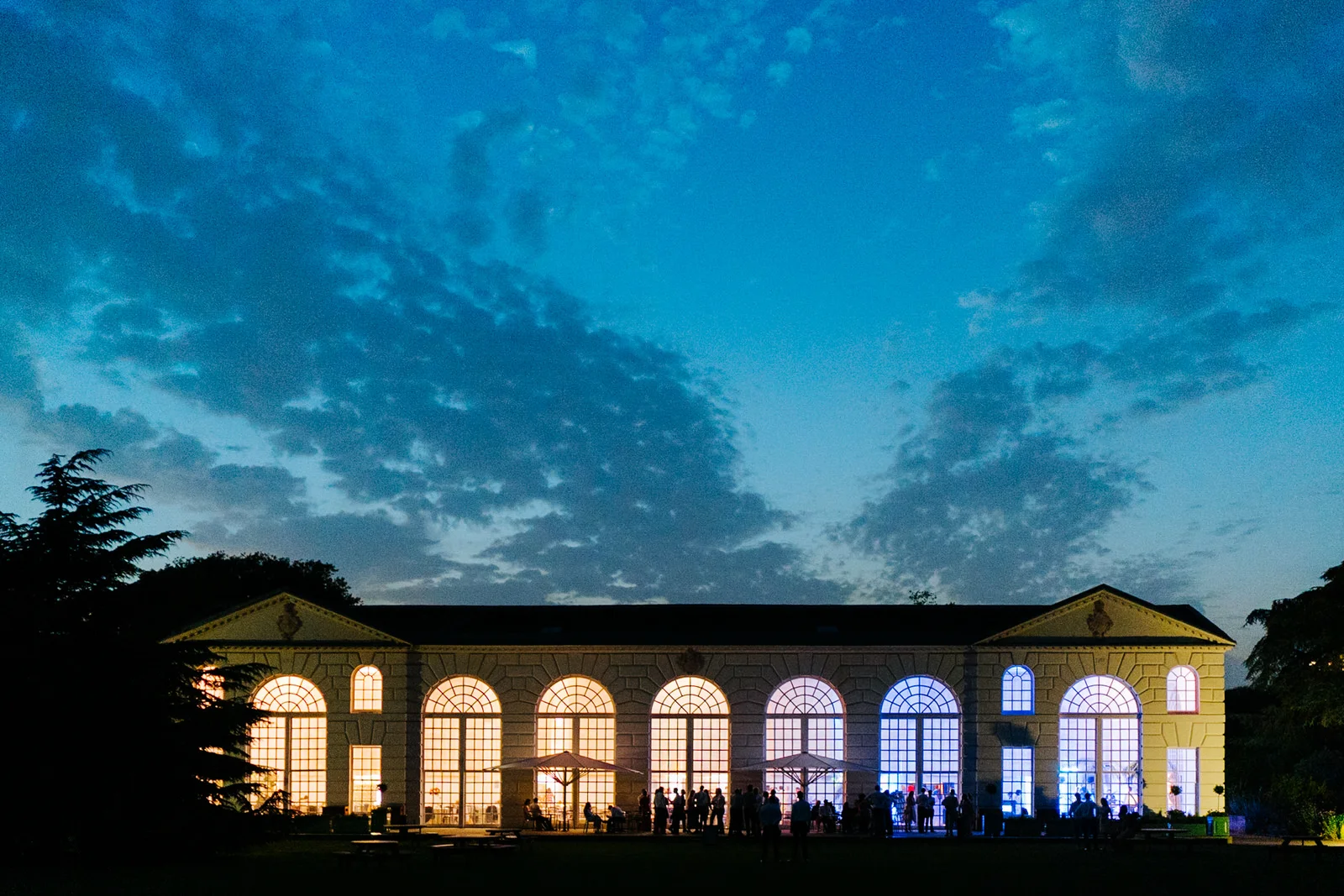 Wide photograph of Nash Conservatory in Kew Gardens as sun sets behind.