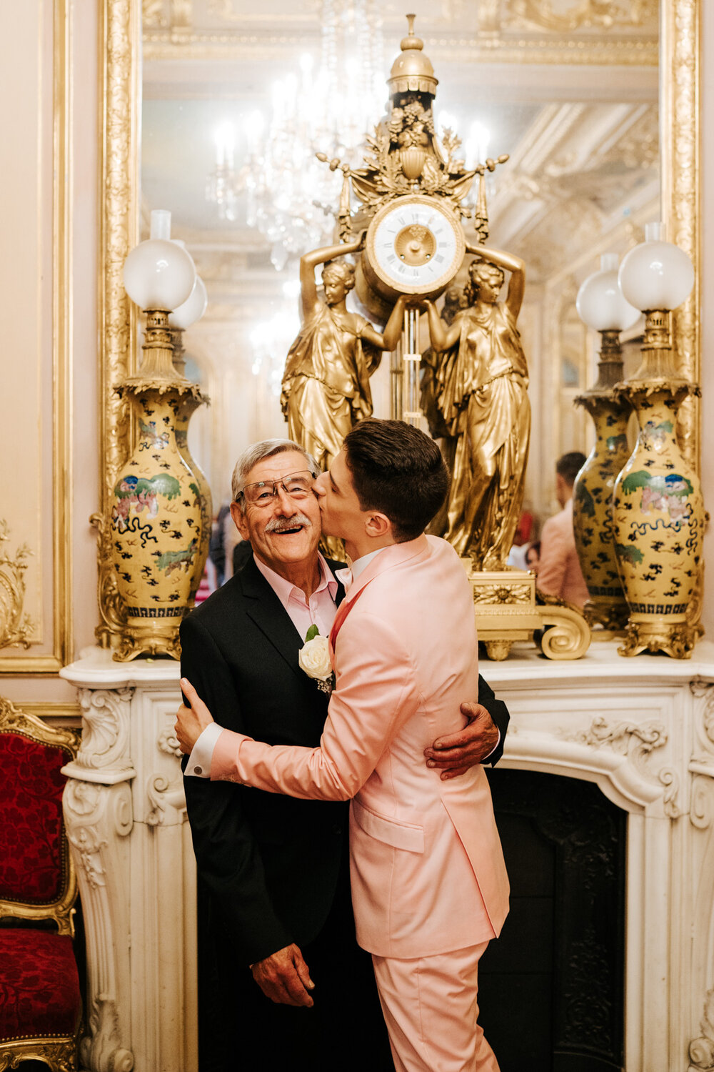  One of the grooms kisses and hugs his grandfather in front of beautiful, large mirror 