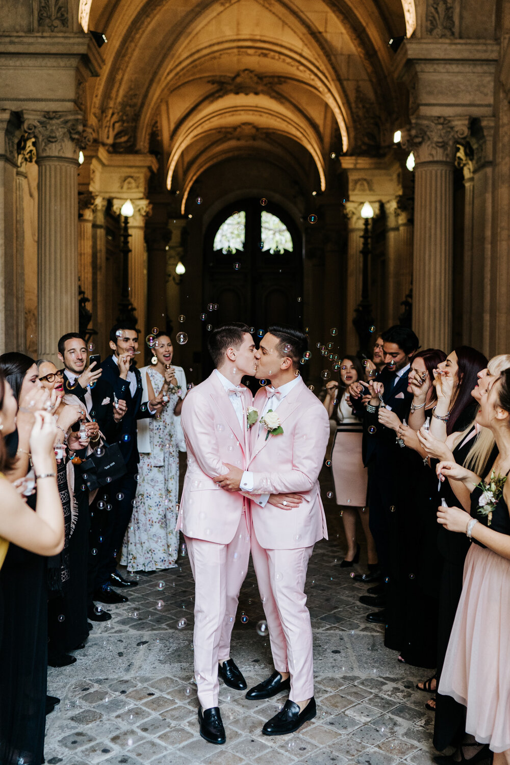  Both grooms kiss in the middle of a bubble tunnel at Paris same sex wedding while family and friends blow bubbles around them 