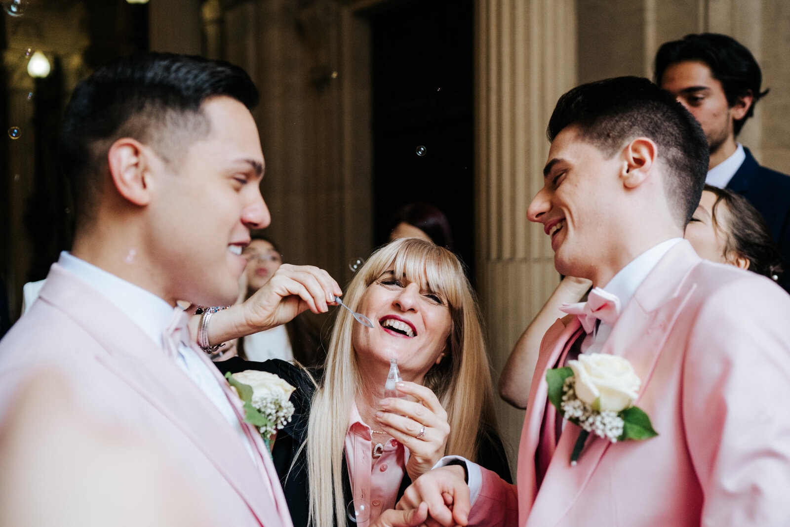  Mother of one of the grooms blows bubbles at newly married couple from up close 