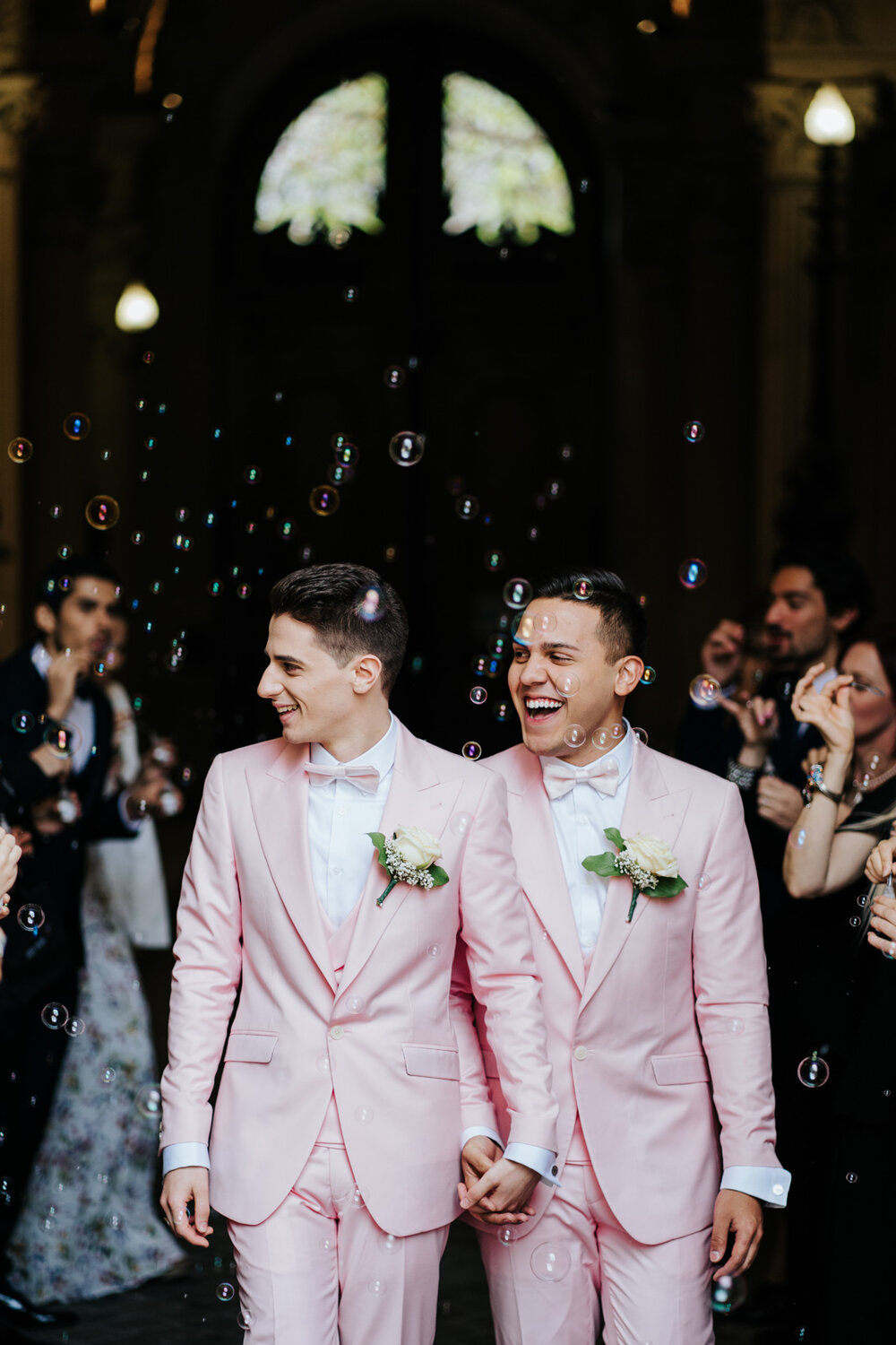  Both grooms walk through the middle of a bubble tunnel at Paris same sex wedding while family and friends blow bubbles around them 