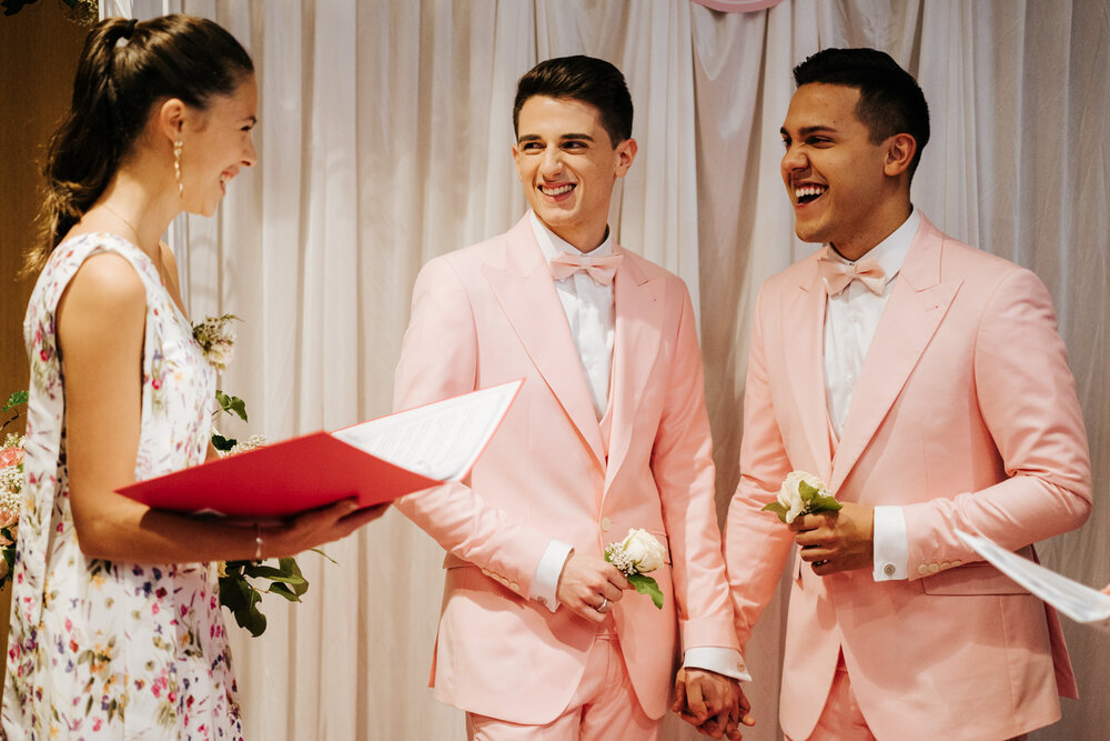  Both grooms hold hands and smile at one of their best friends during same sex wedding in Paris 