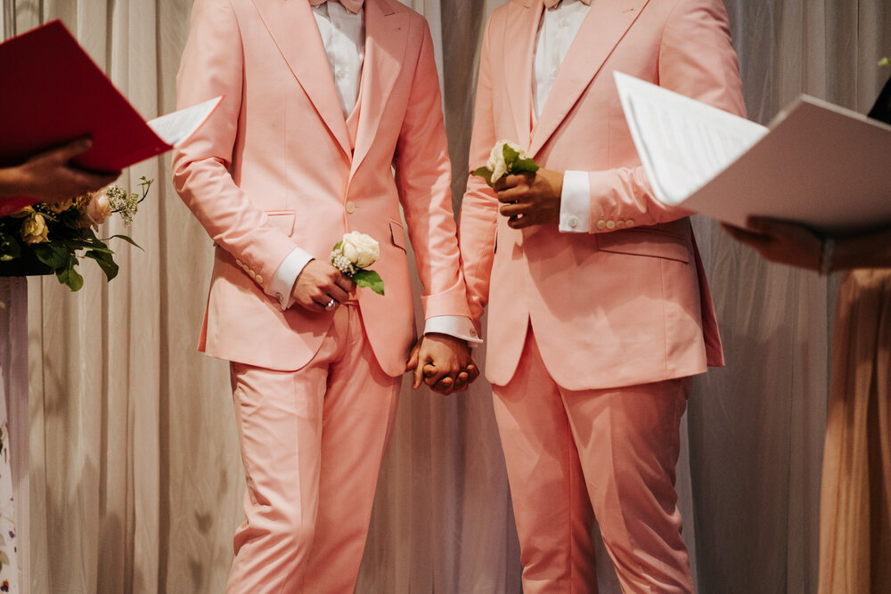  Both grooms hold hands at the front of the aisle as two of their closest friends officiate the ceremony 