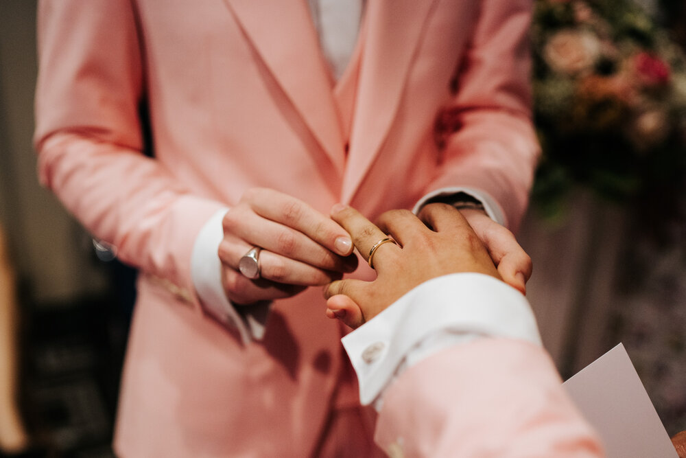  One of the grooms placing the wedding band on the other groom's finger 
