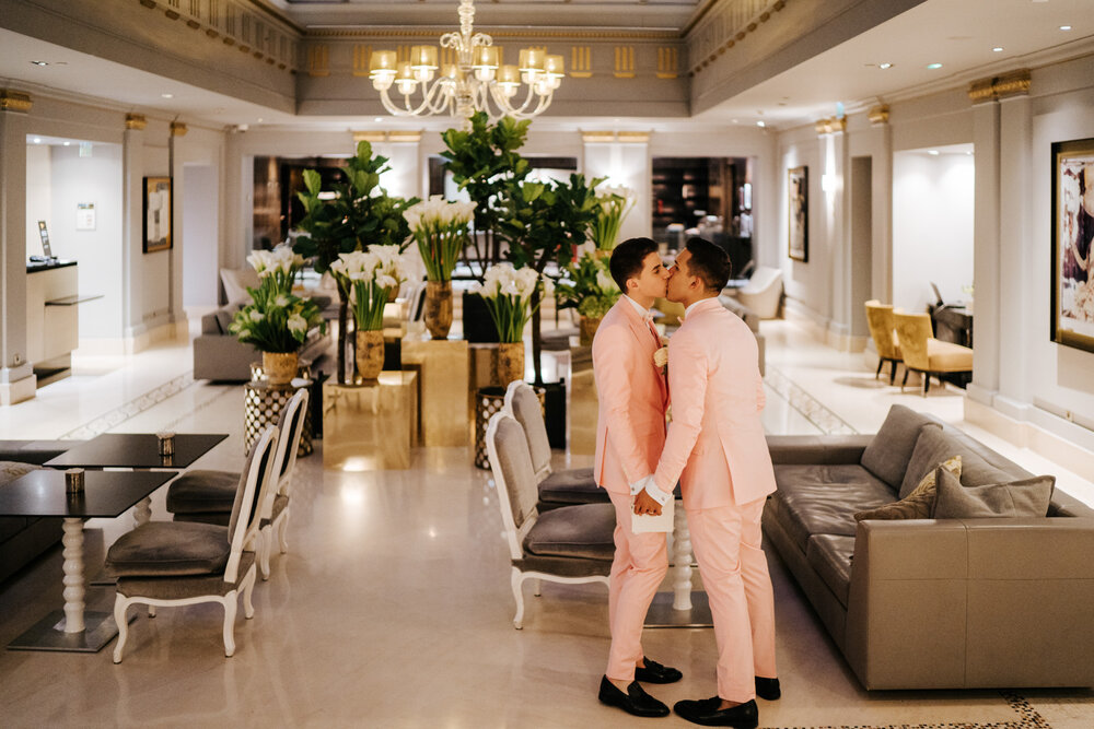 Both grooms sneaking in a kiss in the hotel lobby at Sofitel Paris 