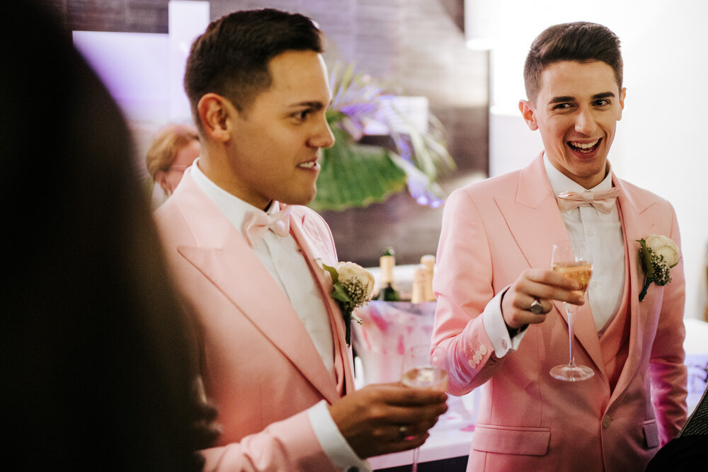  Grooms toasting champagne and smiling at guests during drinks reception at Paris same sex wedding 
