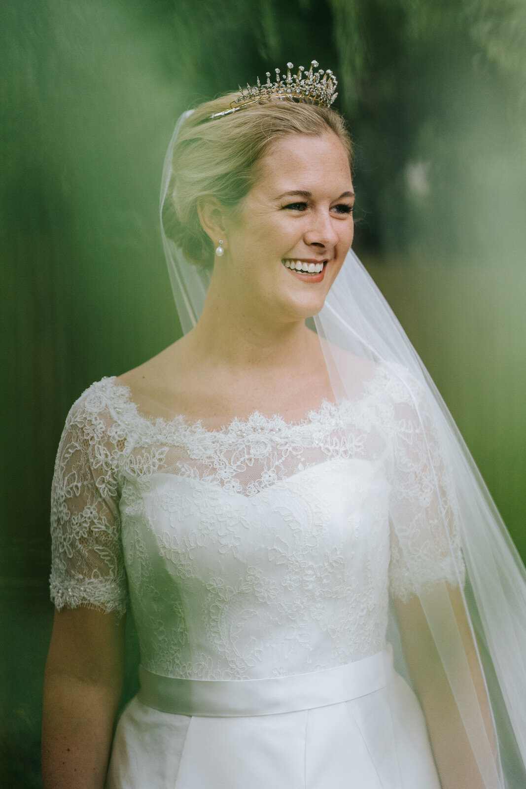 Bride stands behind foliage in her parent's garden before leaving for ceremony